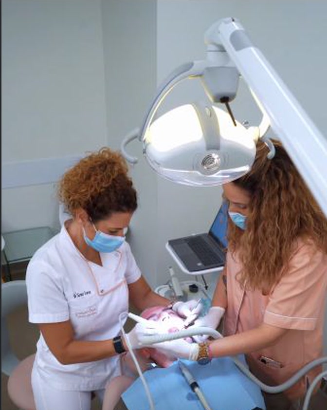 Profissionais da Clínica Dentária Graça Leça equipadas com máscara e luvas junto a equipamento dentário